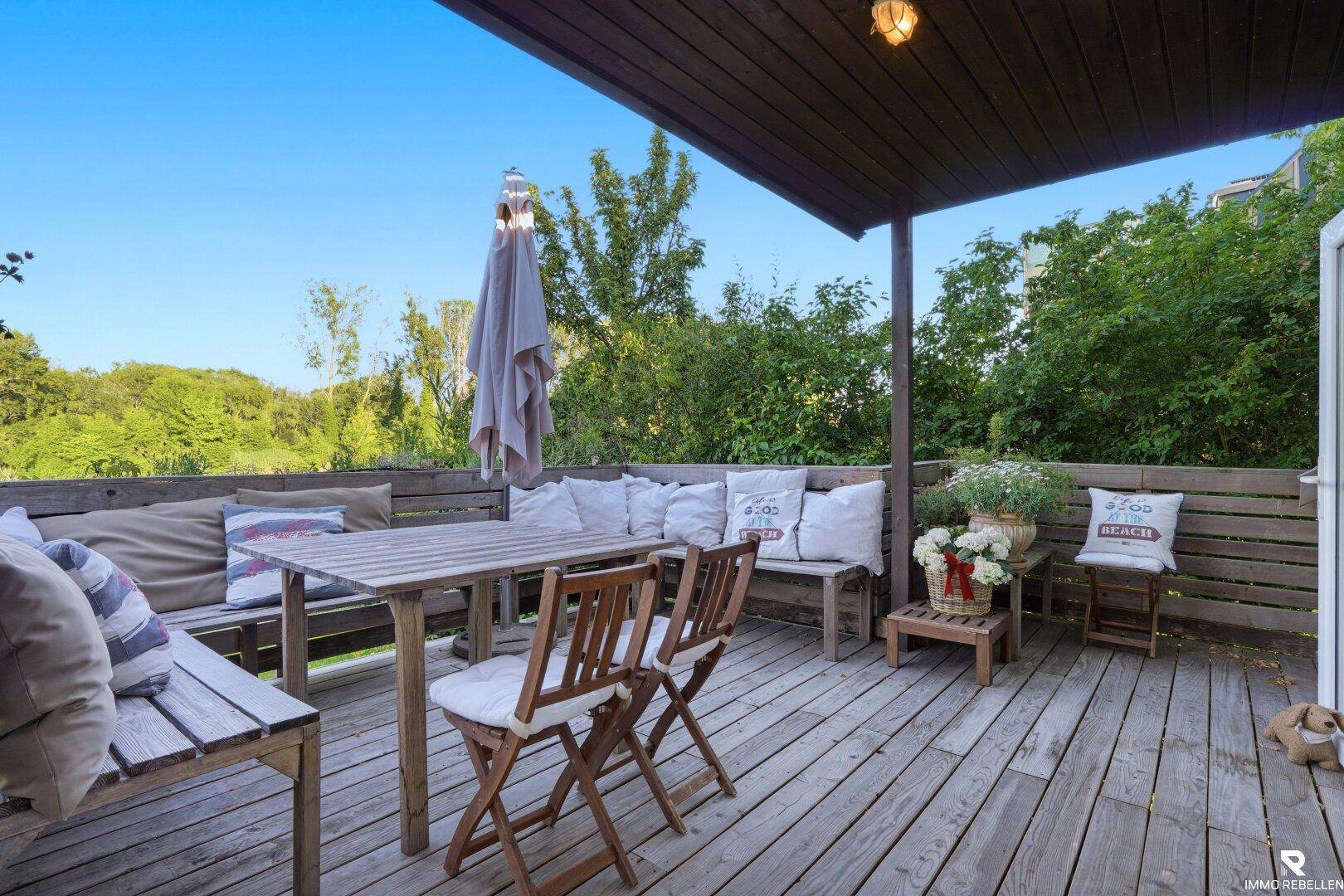 Gemütliche Holzterrasse mit Sitzgelegenheiten, Sonnenschirm und Blick ins Grüne.