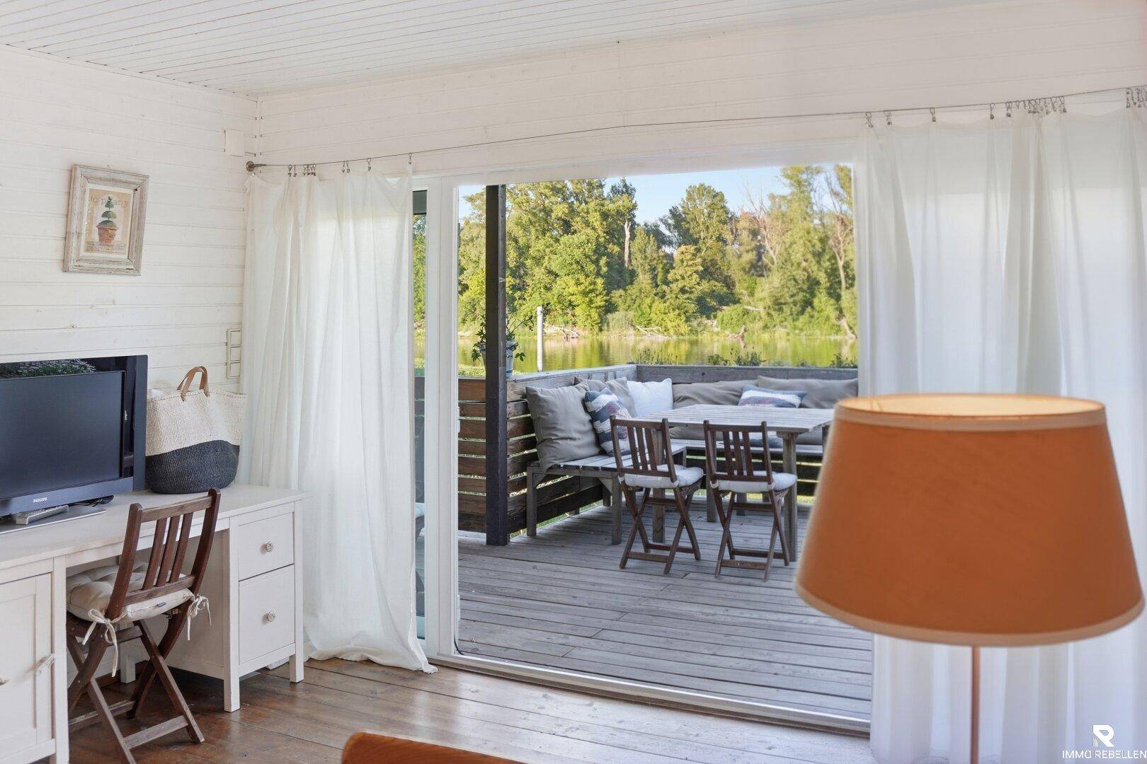 Wohnzimmer mit Blick auf die Terrasse und das Wasser, helle Einrichtung und Holzboden.