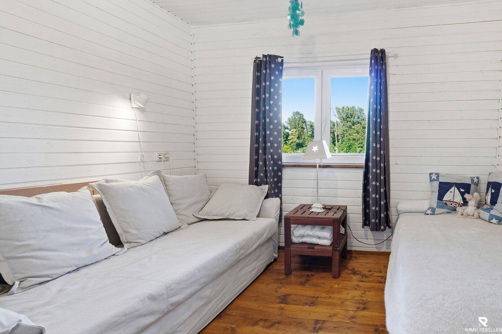 Gemütliches Schlafzimmer mit zwei Betten, Holzboden und einem Fenster mit Blick ins Grüne.