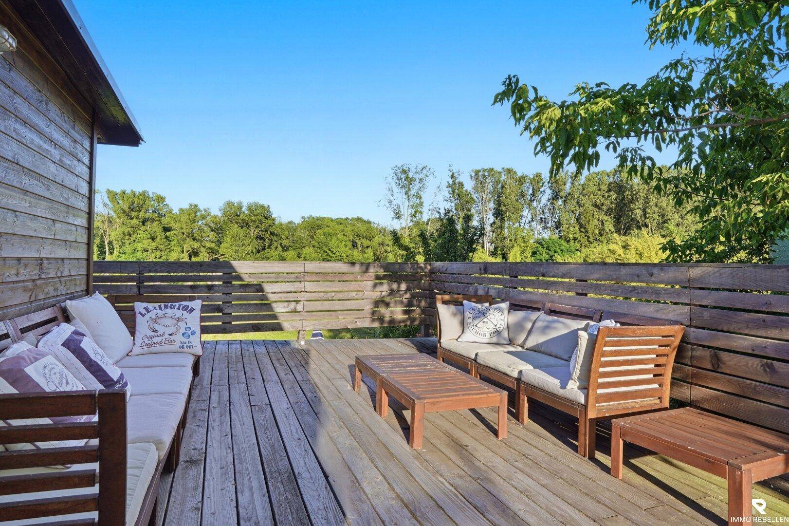 Große Holzterrasse mit bequemen Lounge-Möbeln und Blick auf die umliegende Natur.