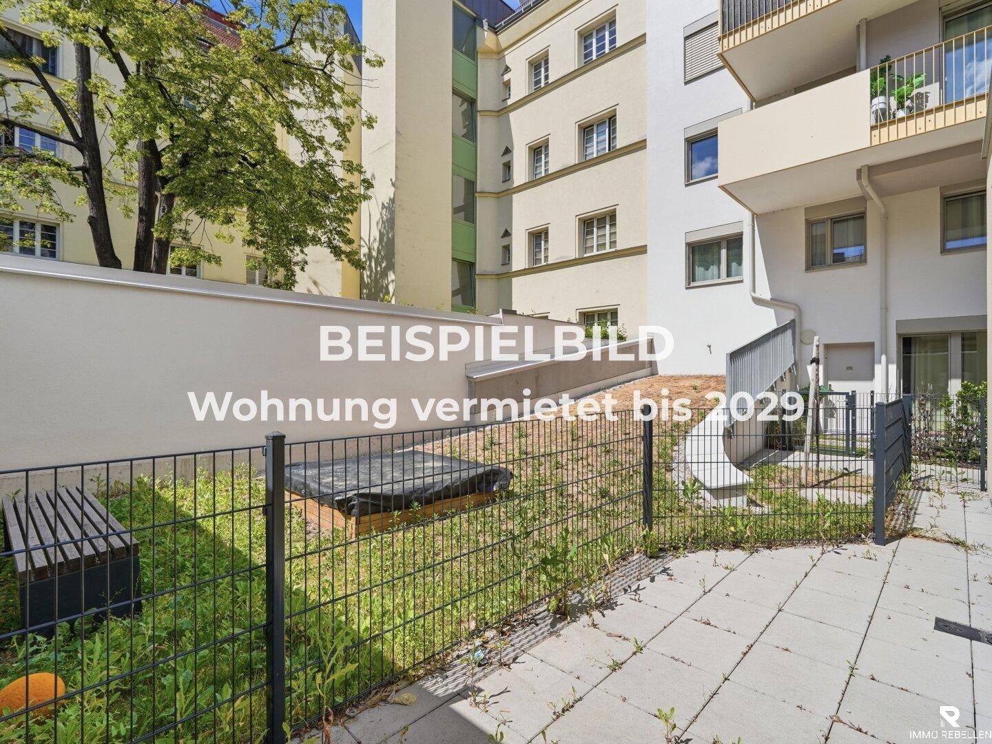 Kleiner, eingezäunter Gartenbereich mit Rasenfläche und Sitzbank im Innenhof der Wohnanlage.