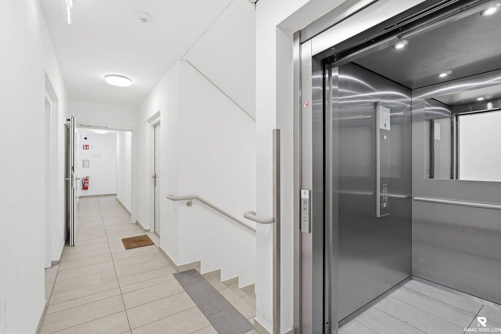 Heller Flur im Gebäude mit modernem Aufzug und Treppenhauszugang.