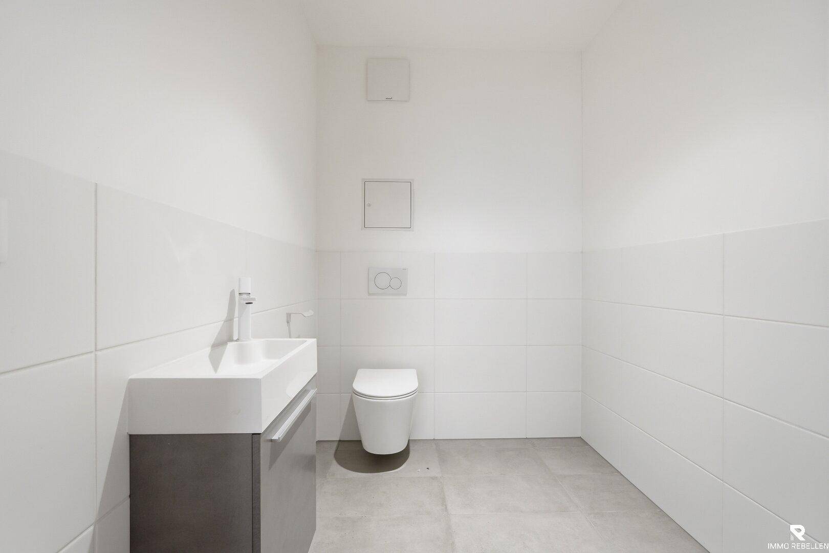 Schlichtes Gäste-WC mit weißen Fliesen, wandhängender Toilette und modernem Waschtisch.