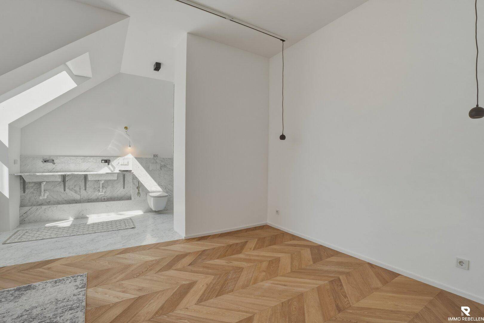 Heller Schlafbereich mit Fischgrätparkett und offenem Übergang zum Badezimmer.