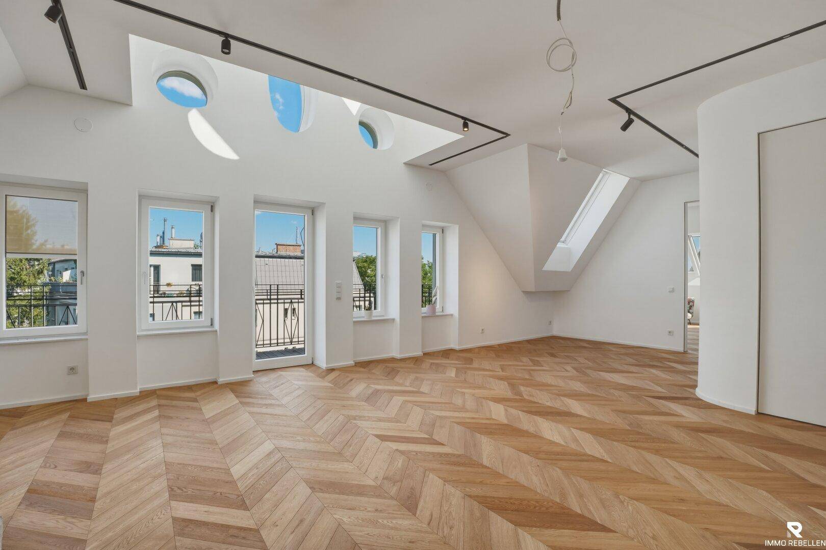 Heller Raum mit Dachschrägen, Fischgrätparkett und Zugang zu einem französischen Balkon.