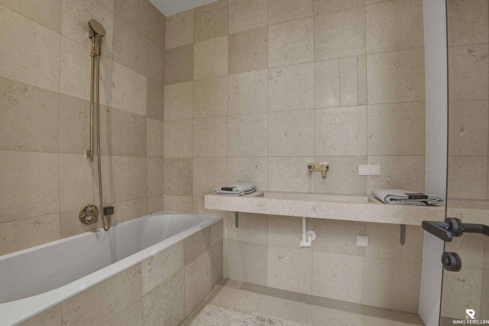 Modernes Badezimmer mit beigefarbenen Fliesen, Badewanne und schwebendem Waschtisch.