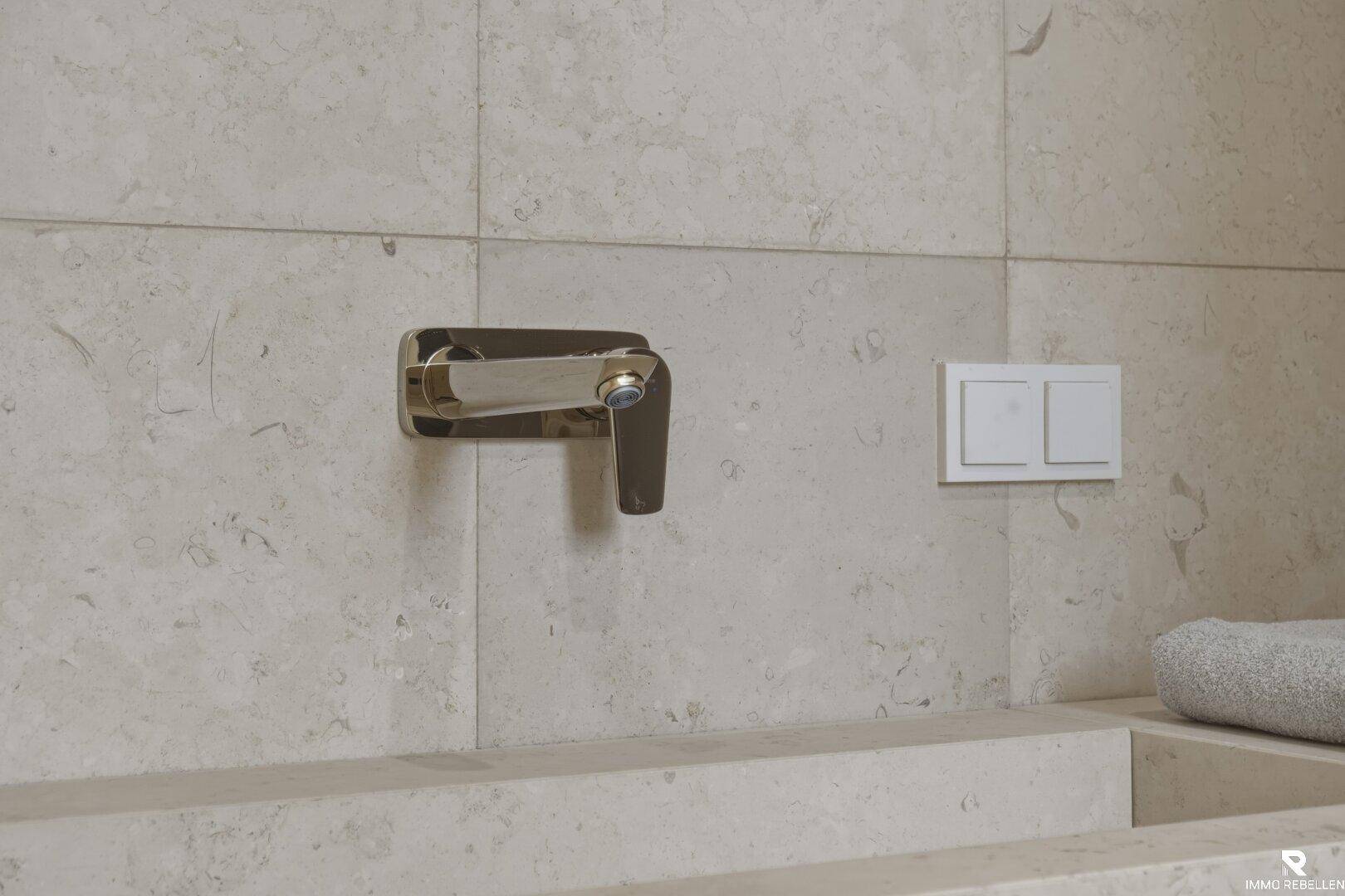 Moderne Armatur über dem Waschtisch mit beigefarbenen Fliesen im Badezimmer.