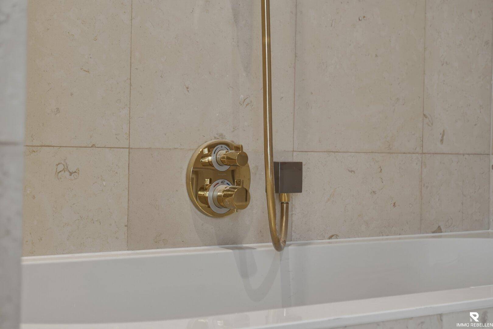 Detailaufnahme der modernen Armatur in Goldoptik über der Badewanne.