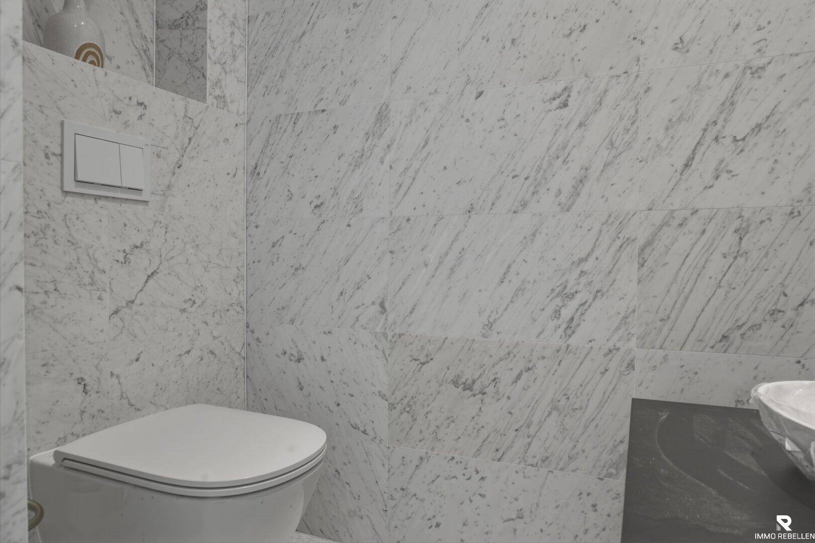 Modernes WC mit wandmontierter Toilette und eleganten Marmorfliesen an den Wänden.
