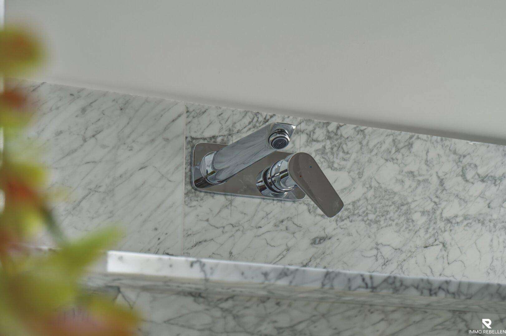 Detailaufnahme einer modernen Armatur an der Marmorwand im Badezimmer.