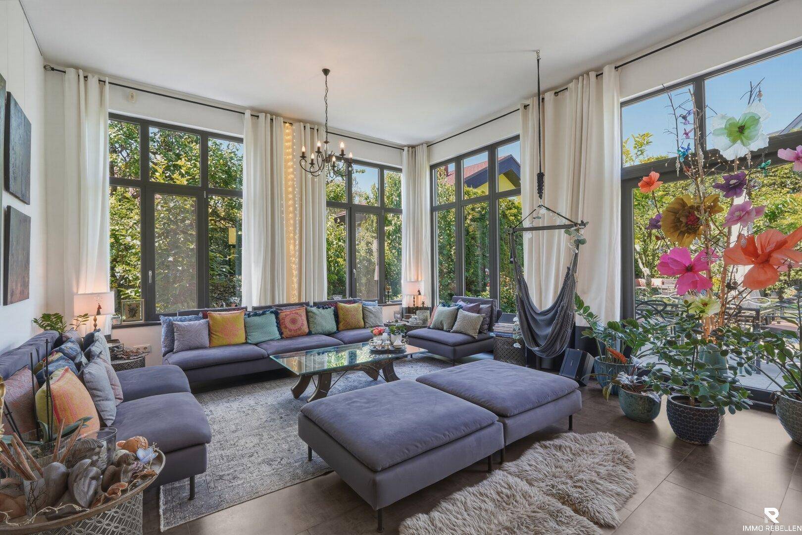 Lichtdurchflutetes Wohnzimmer mit großen Fenstern, bequemen Sofas und farbenfroher Dekoration.