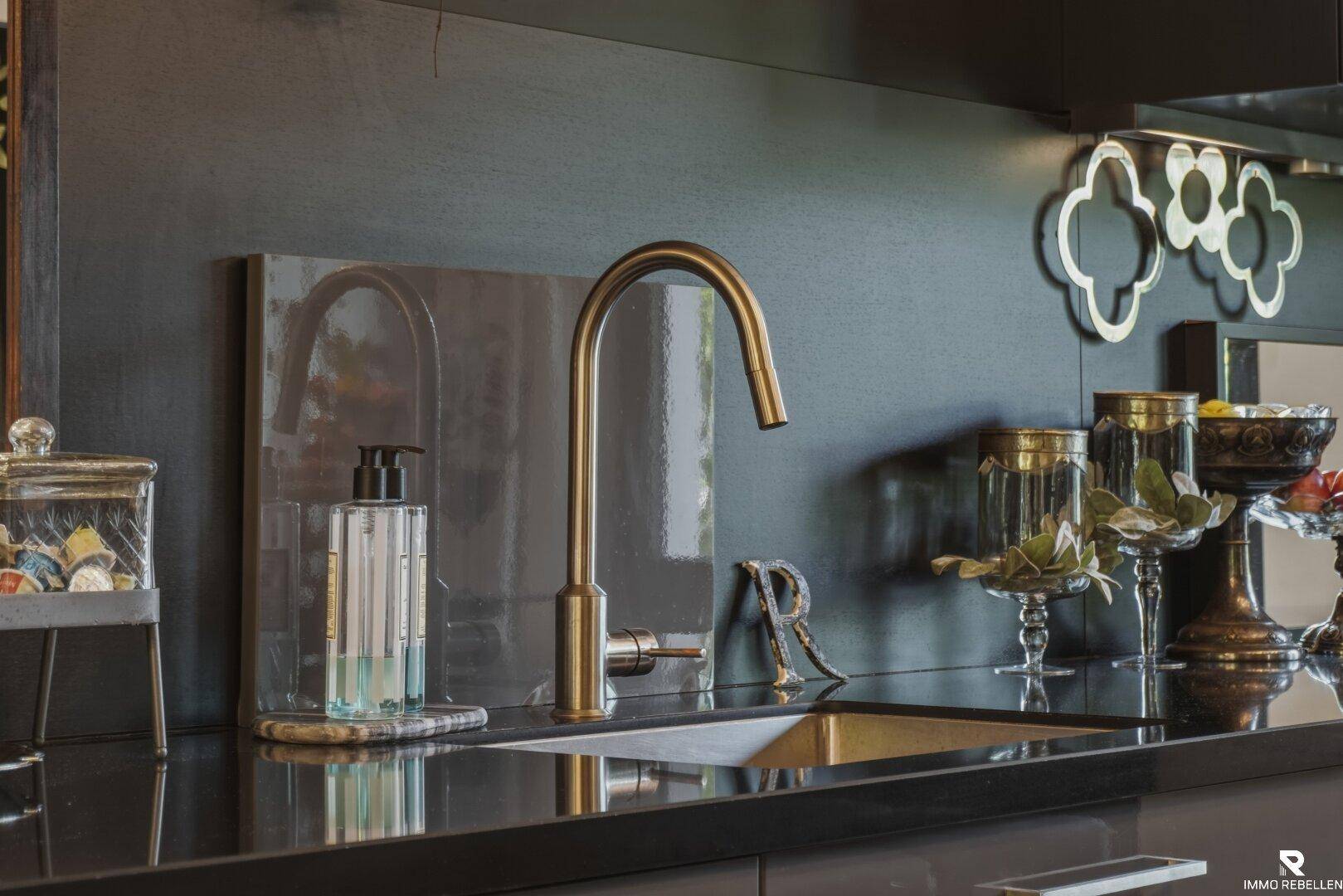 Elegantes Spülbecken mit goldfarbenem Wasserhahn und dunkler Arbeitsplatte in einer modernen Küche.