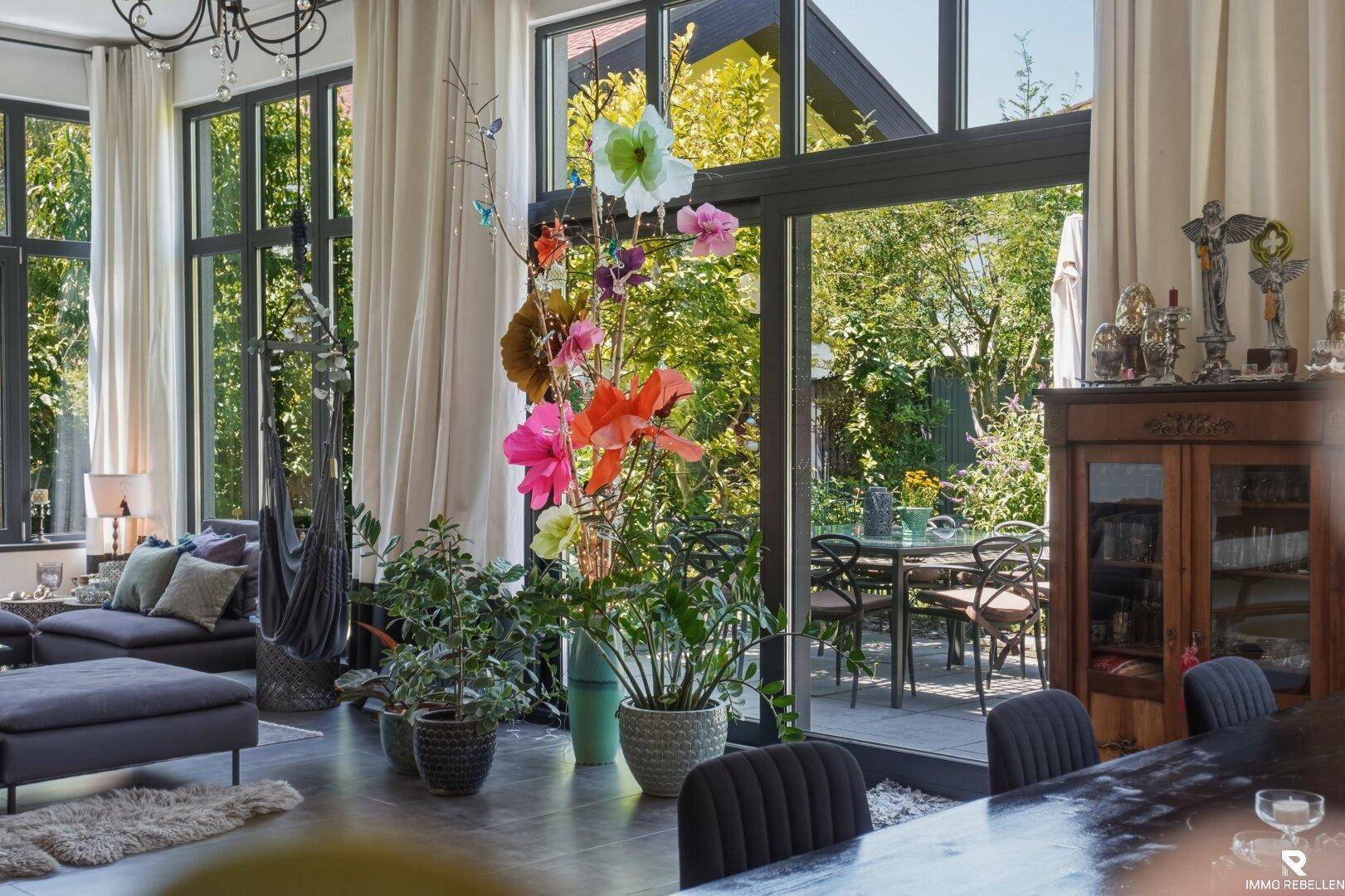 Heller Wohn- und Essbereich mit großen Fenstern und Zugang zur Terrasse, umgeben von viel Grün.