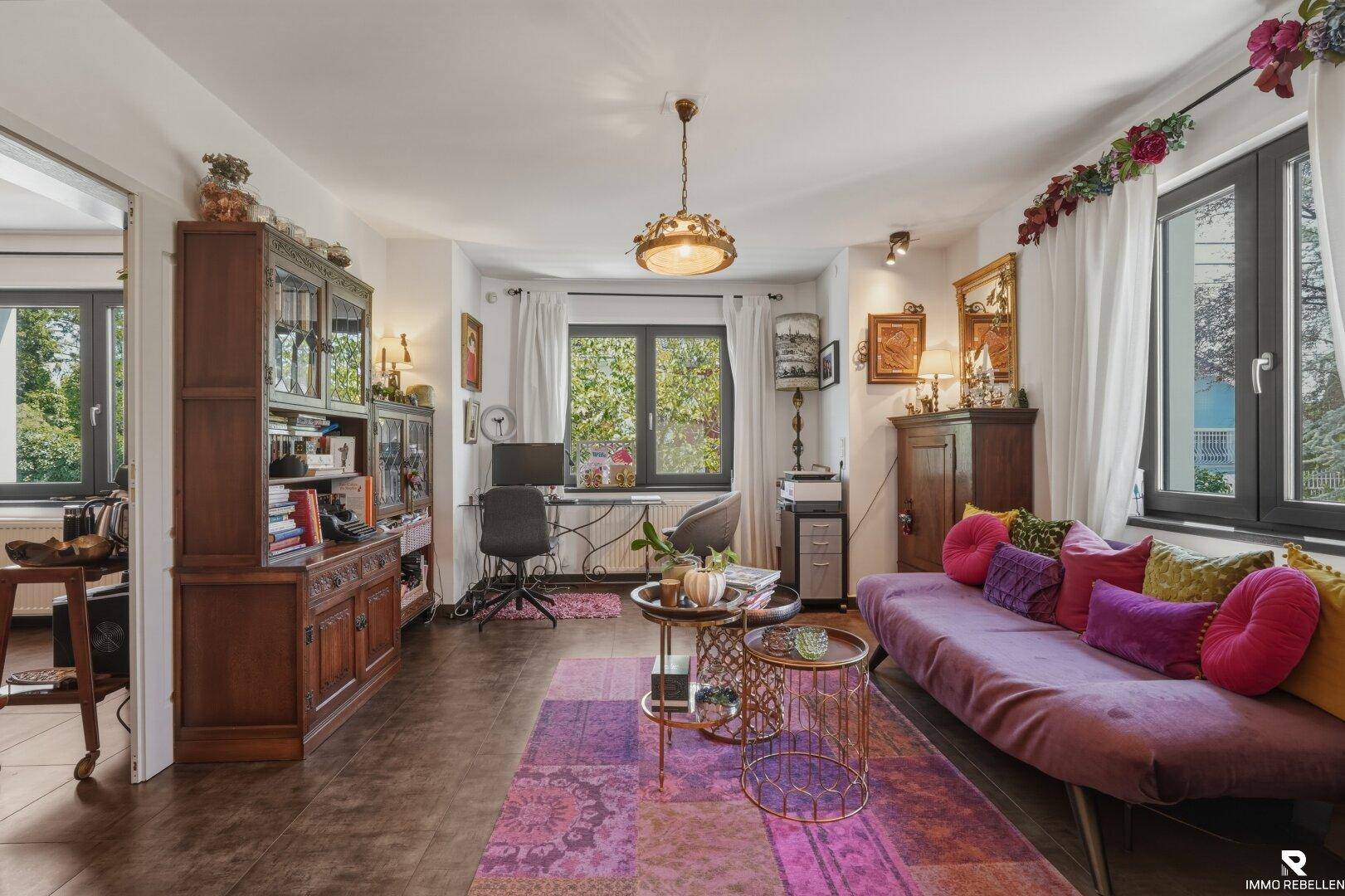 Helles Wohnzimmer mit Sofa, Schreibtischbereich und traditionellen Holzmöbeln, die eine warme Atmosphäre schaffen.