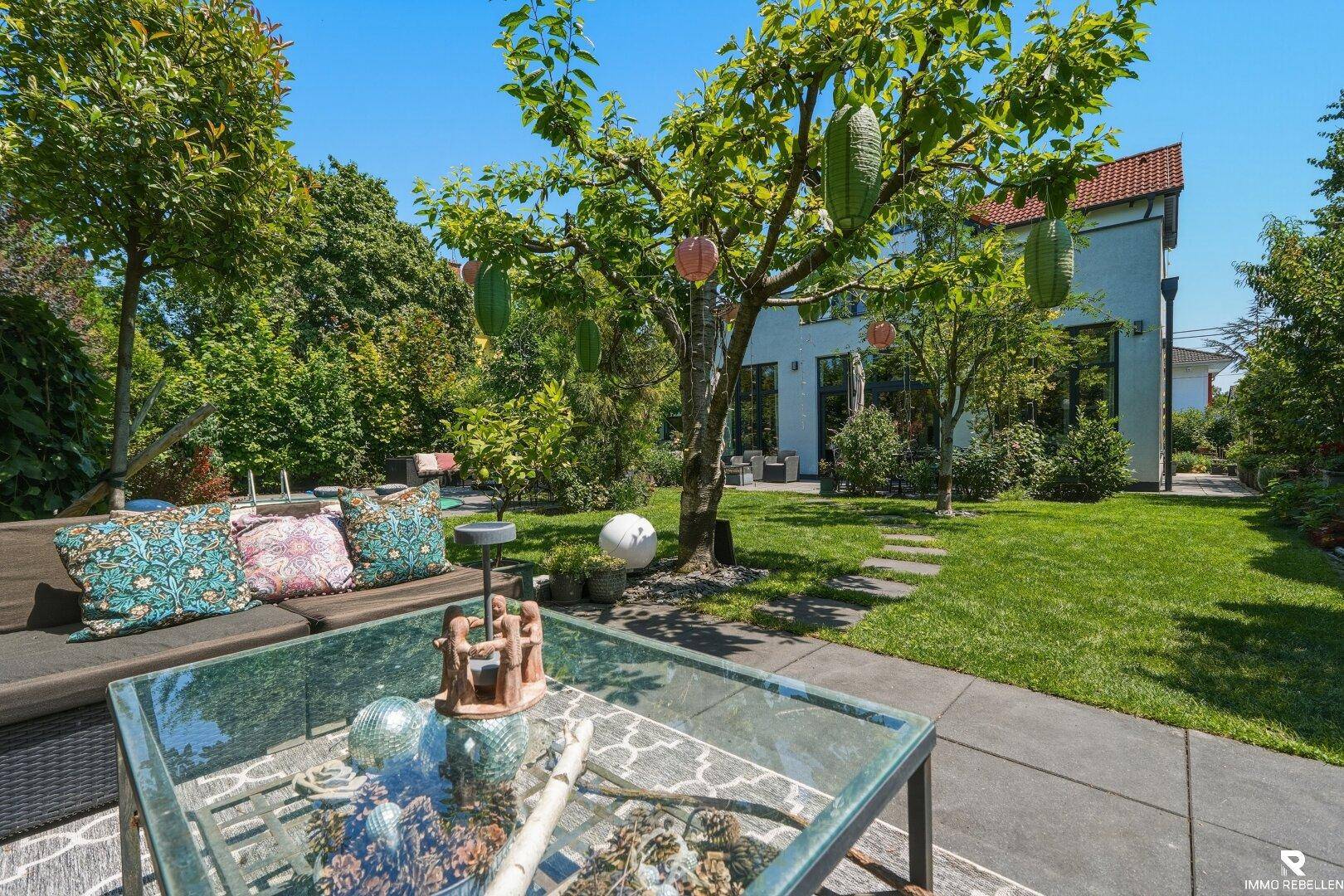 Gepflegter Garten mit gemütlicher Sitzecke und Blick auf das moderne Haus mit großen Fenstern.