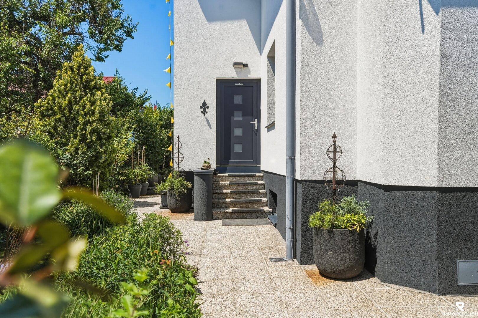 Eingangsbereich des Hauses mit Stufen und dekorativen Topfpflanzen, die eine einladende Atmosphäre schaffen.