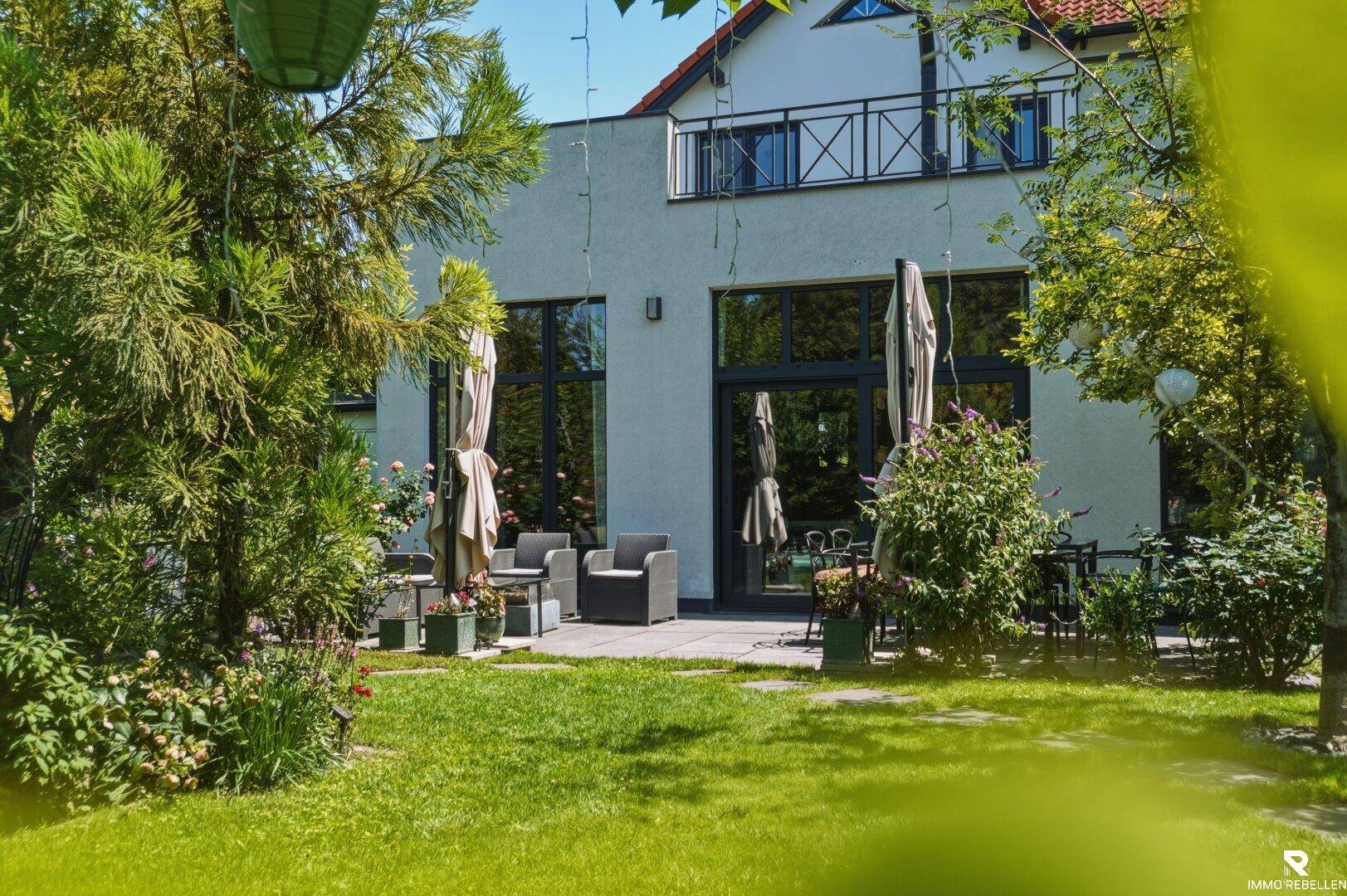 Weitläufiger Garten mit Rasenfläche und Terrasse, umgeben von Bäumen und Sträuchern.