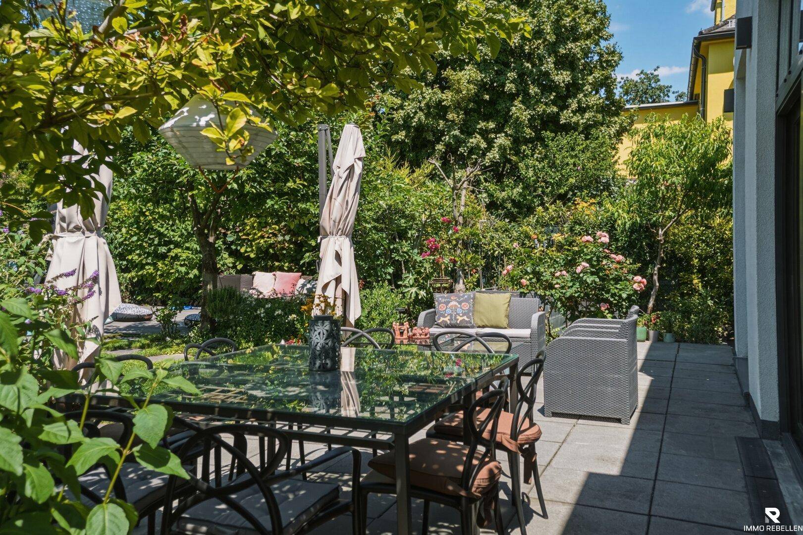 Gemütliche Terrasse mit Esstisch und Lounge-Möbeln, umgeben von viel Grün und Bäumen.