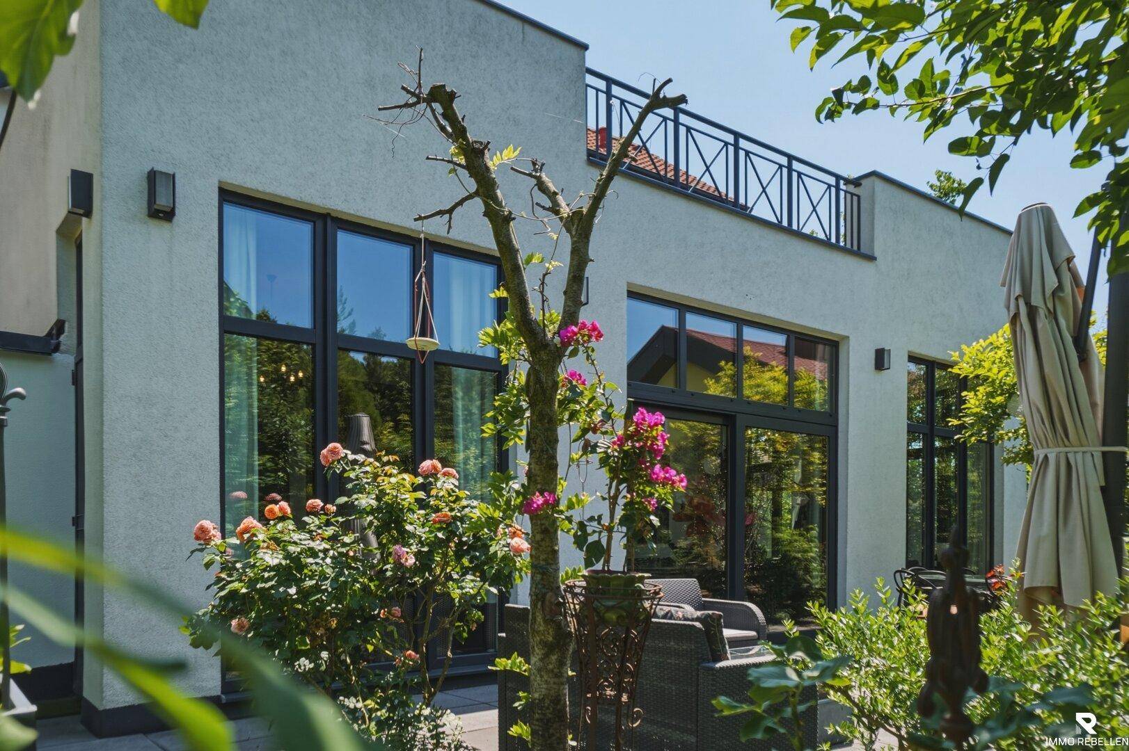 Rückseite des Hauses mit großer Terrasse und bodentiefen Fenstern, die viel Licht hereinlassen.