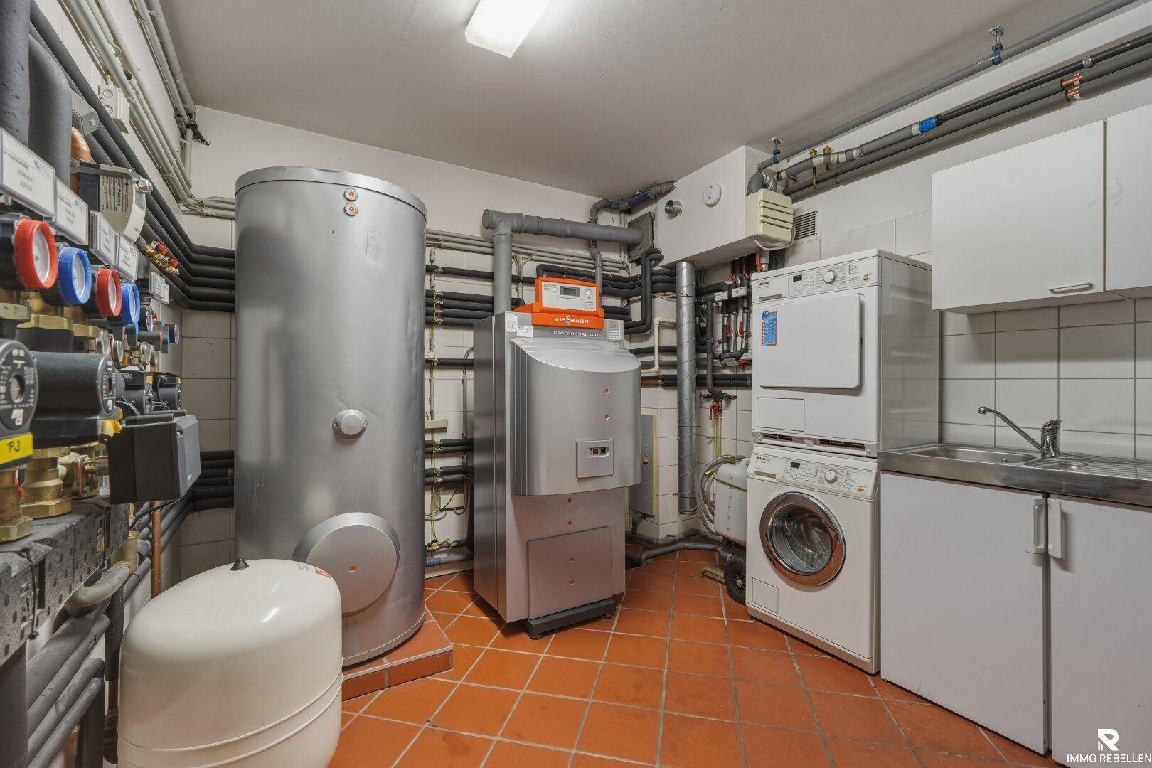 Funktionaler Hauswirtschaftsraum im Keller mit Heizungsanlage, Waschmaschine, Trockner und Fliesenboden.