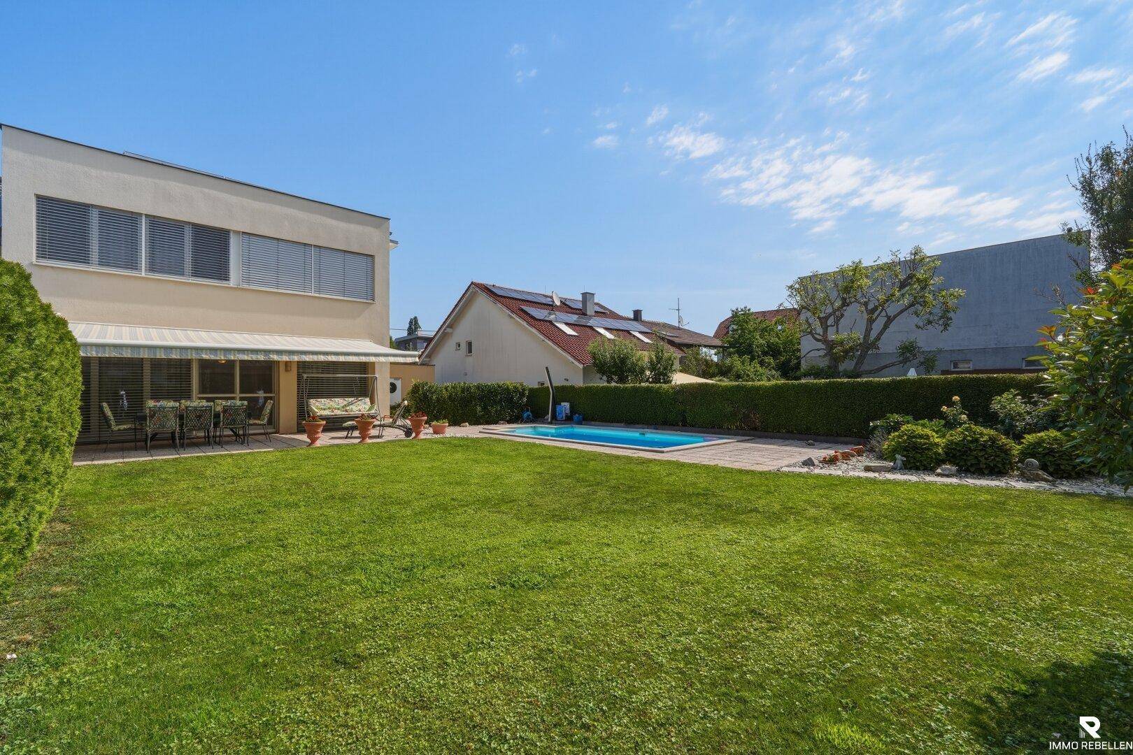 Sonniger Garten mit Pool, weitläufiger Rasenfläche und Blick auf die moderne Hausfassade.