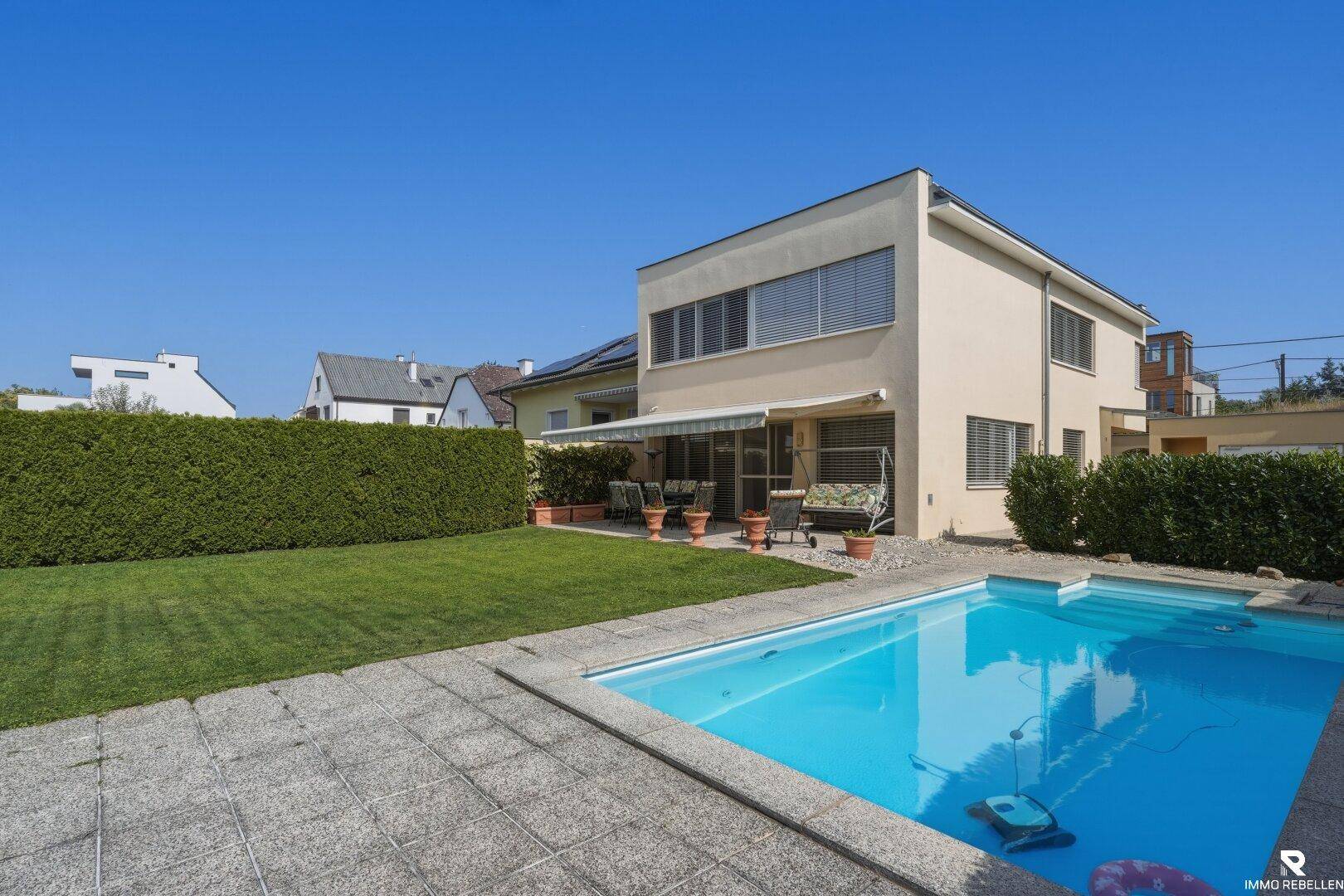 Großer Garten mit Rasenfläche, Swimmingpool und gepflastertem Bereich neben dem Haus.