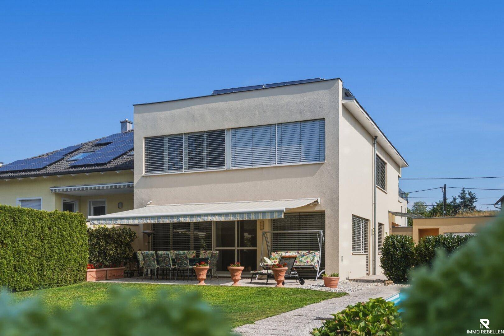 Rückseite des Hauses mit einer überdachten Terrasse, Gartenmöbeln und einem gepflegten Rasenbereich.