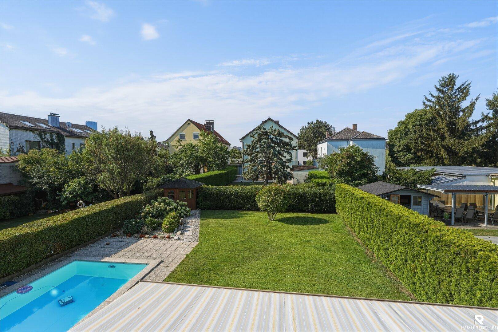 Weitläufiger Garten mit Pool, Rasenfläche und Hecken, umgeben von weiteren Wohnhäusern.