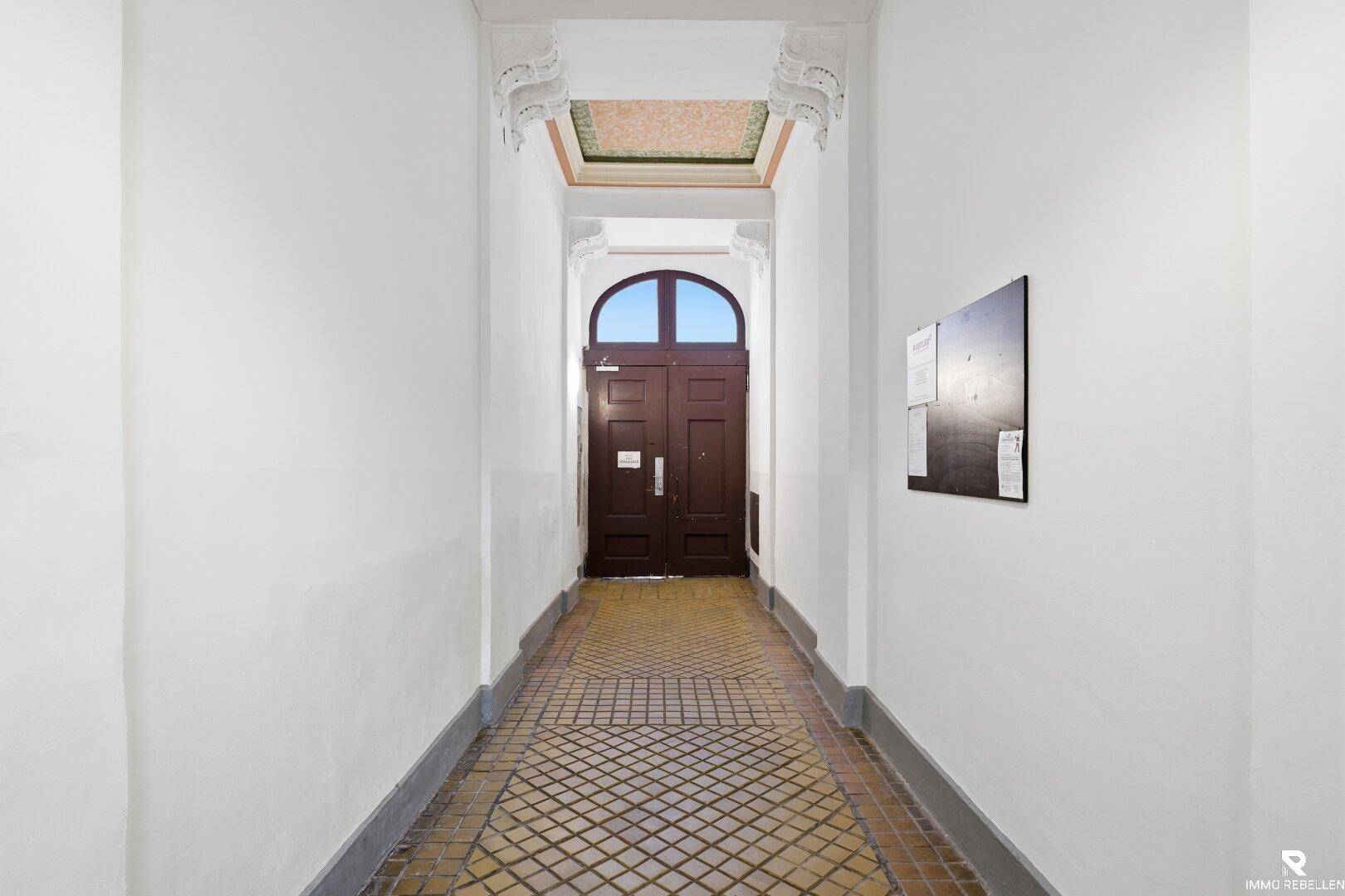 Historischer Eingangsbereich mit gemustertem Fliesenboden und einer verzierten Decke.