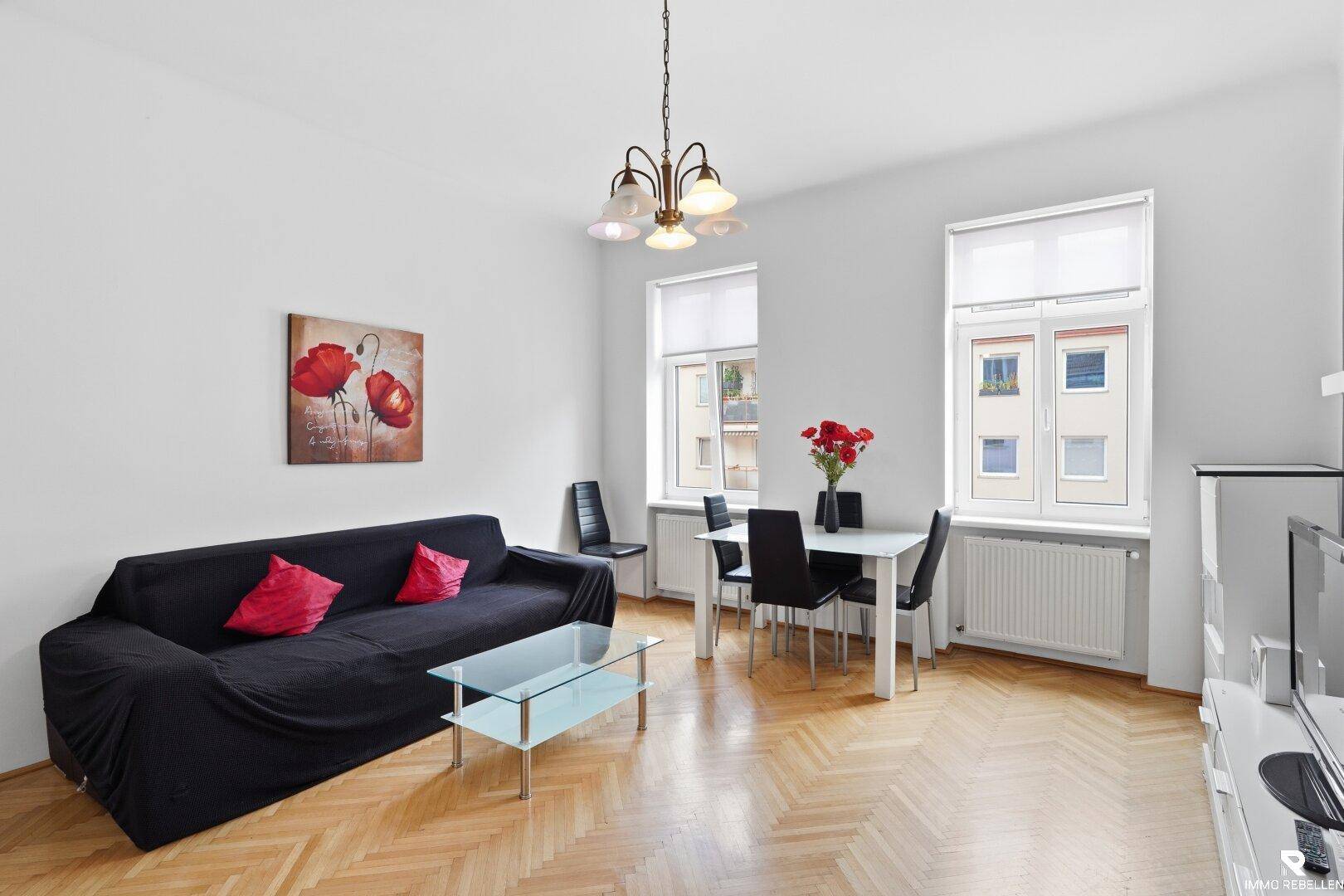 Heller Wohn- und Essbereich mit Fischgrätparkett, einem Sofa und einem Esstisch.