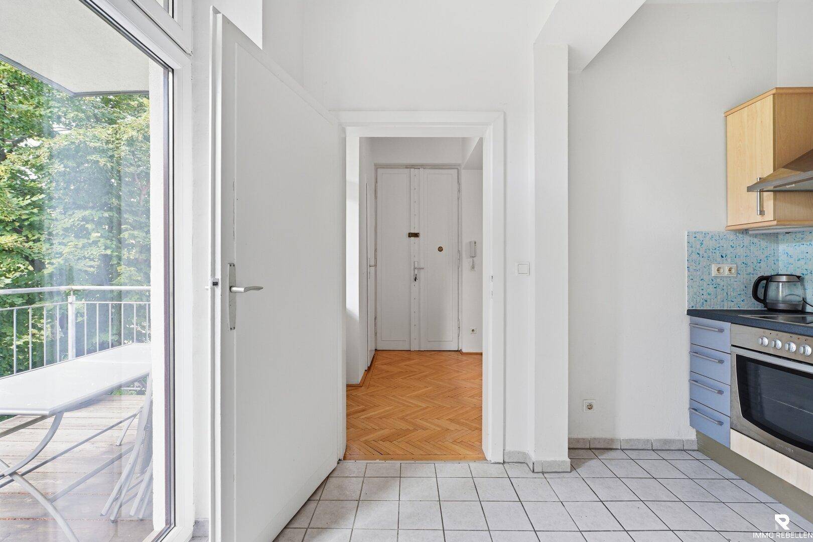 Küche mit Zugang zum Balkon, ausgestattet mit hellen Holzschränken und Fliesenboden.