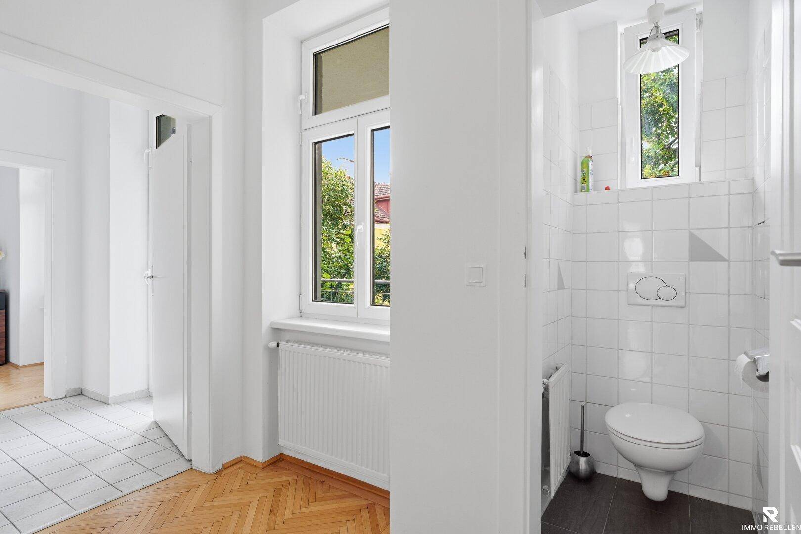Separates WC mit Fenster, weißen Fliesen und einer modernen Toilette.