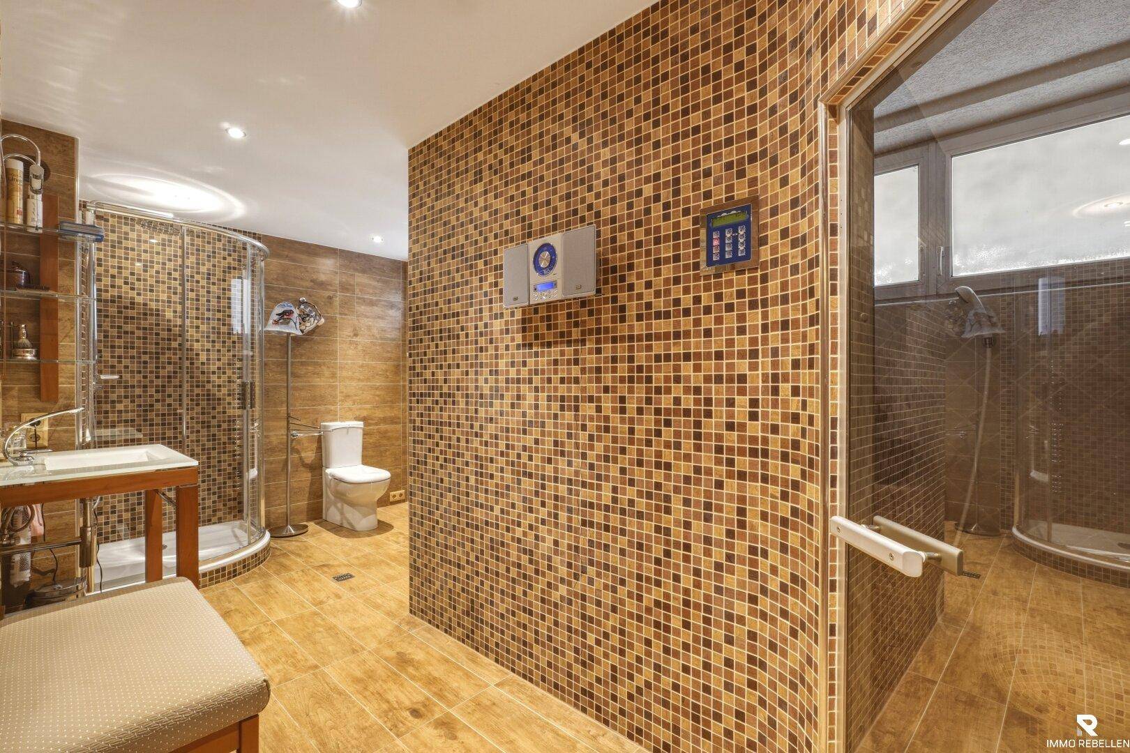 Luxuriöses Badezimmer mit Mosaikfliesen, Dusche und Zugang zu einem Wellnessbereich.