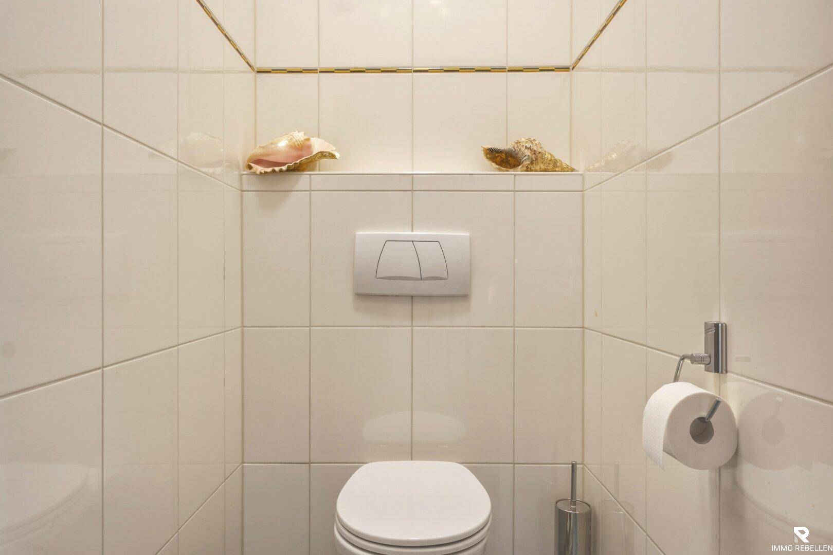Separate Toilette mit weißen Wandfliesen und einem wandhängenden WC für einfache Reinigung.
