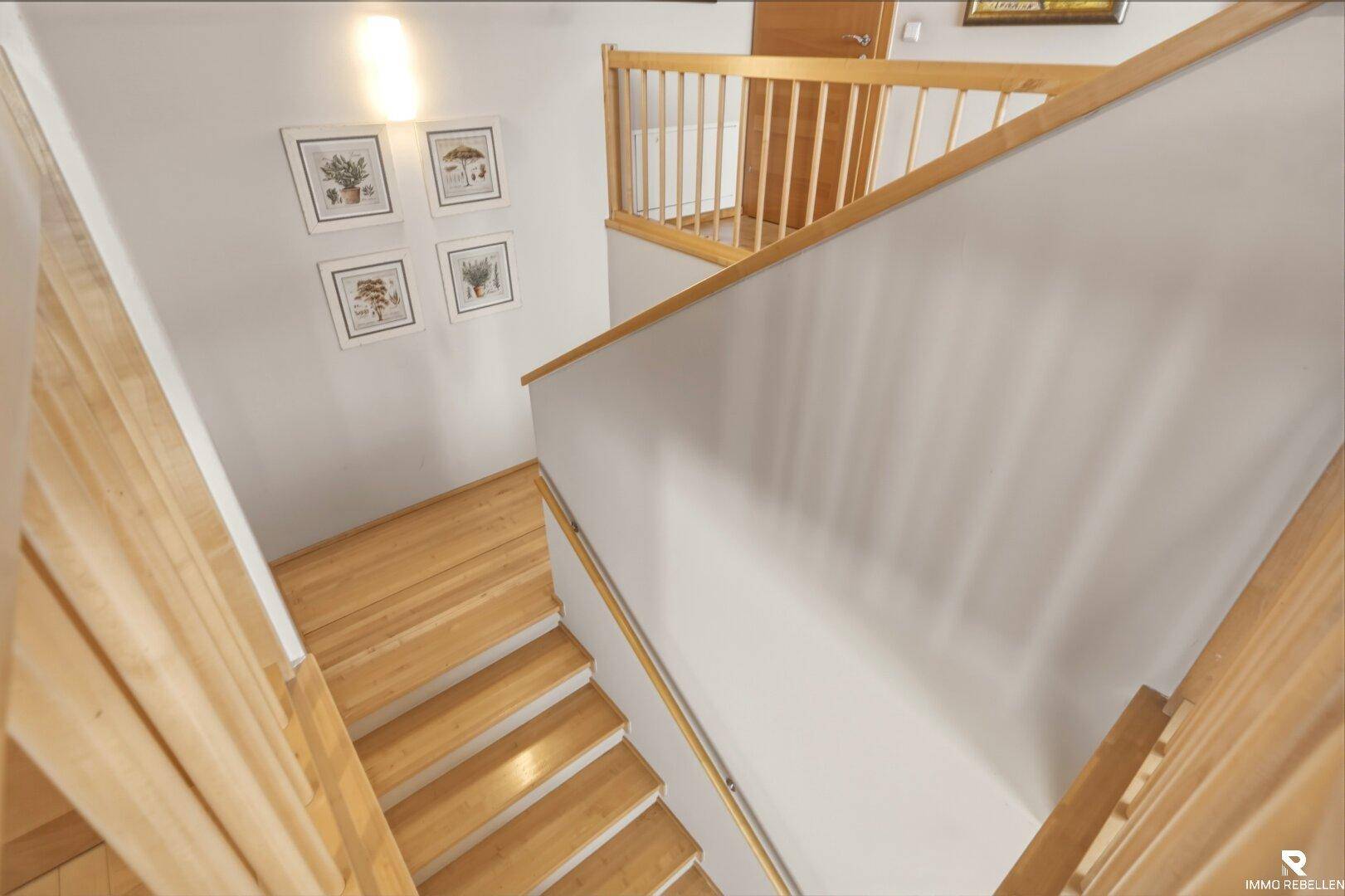Heller Treppenaufgang mit Holzgeländer und Holzboden, der die verschiedenen Etagen verbindet.
