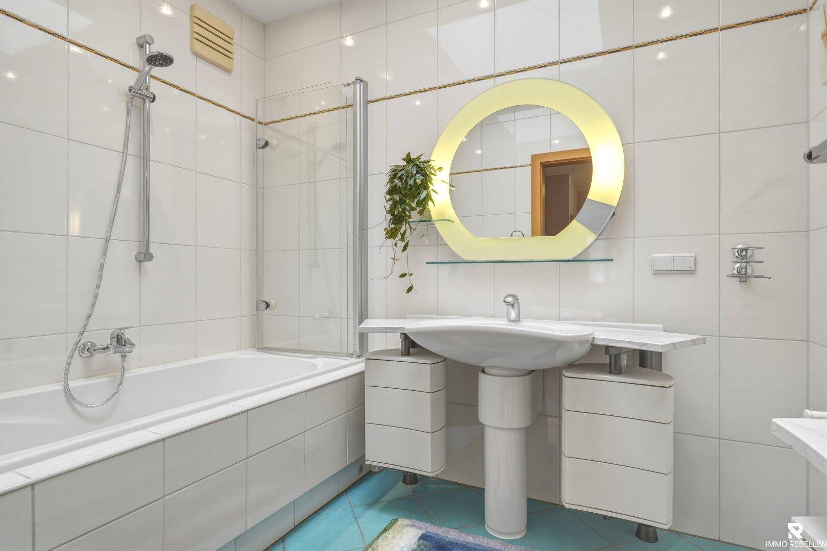 Helles Badezimmer mit weißen Fliesen, Badewanne mit Dusche und modernem Waschtisch.