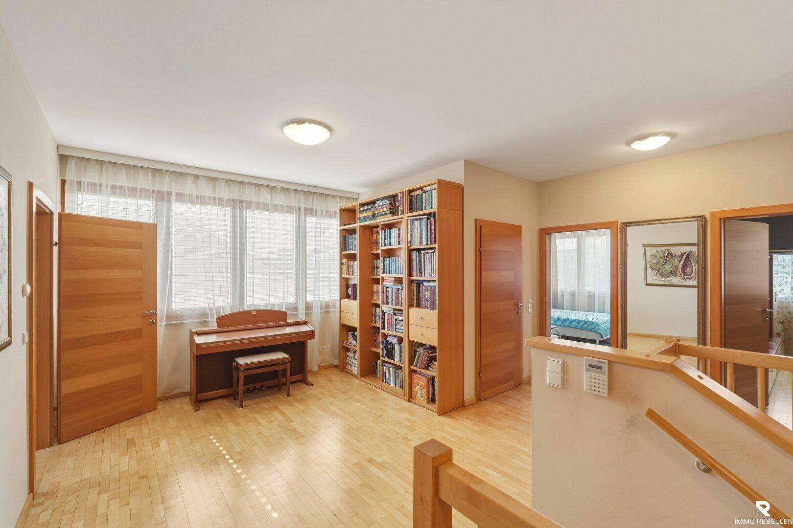 Geräumiger Flur im Obergeschoss mit Holzboden, Bücherregal und Zugang zu mehreren Zimmern.