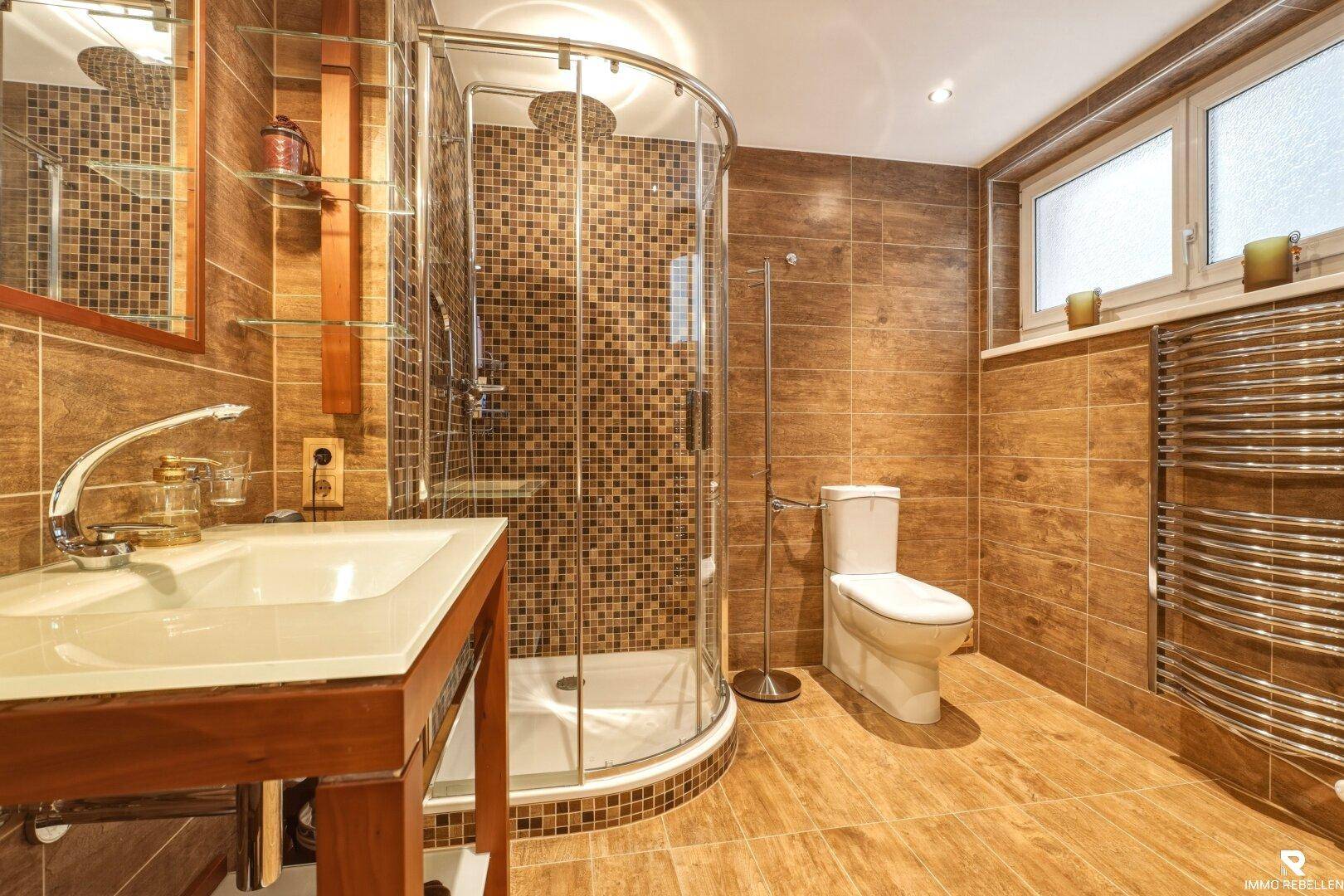Modernes Badezimmer mit braunen Fliesen, Duschkabine, WC und beheiztem Handtuchhalter.