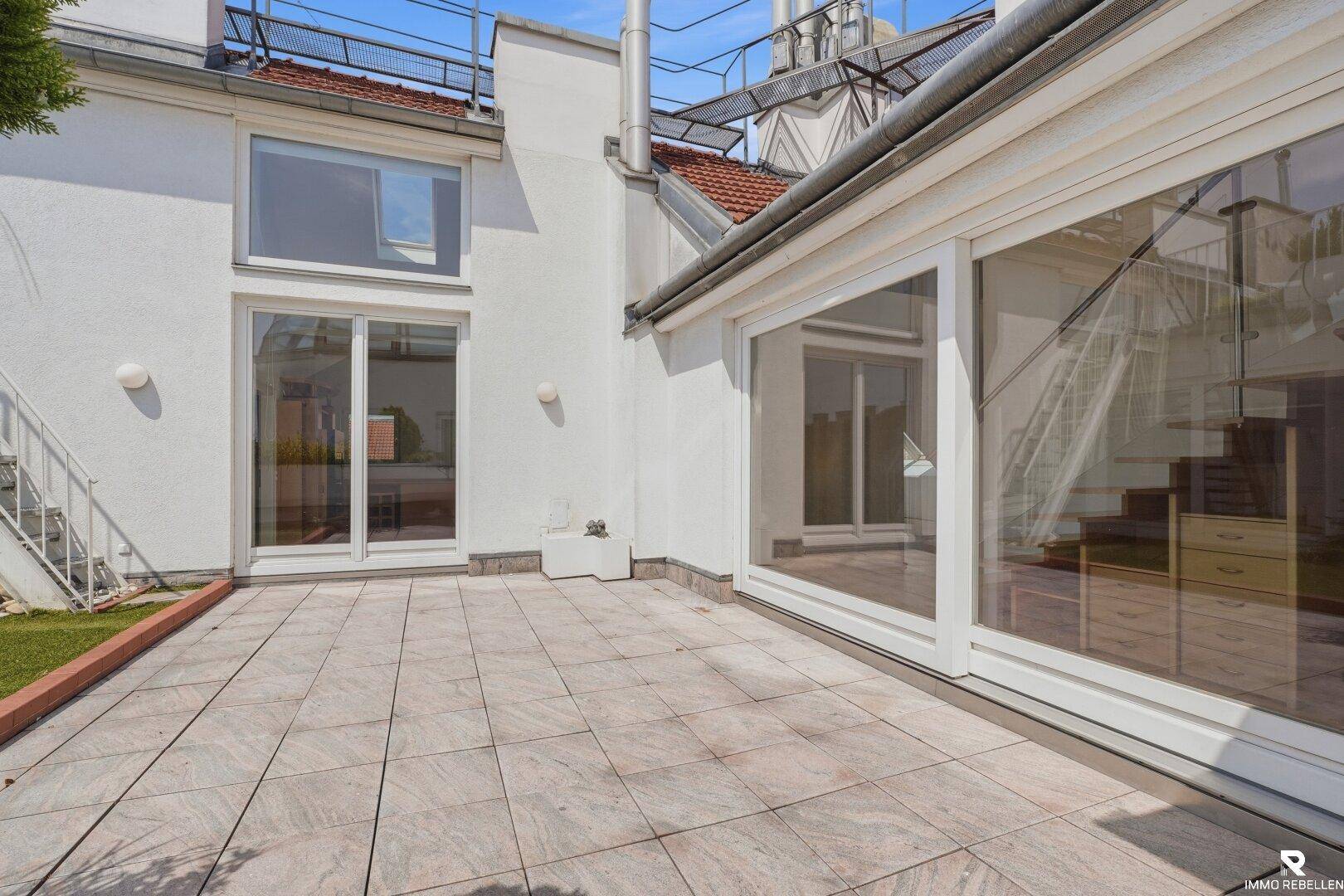 Geräumige geflieste Terrasse mit großen Fenstern und Blick auf die umliegenden Gebäude.