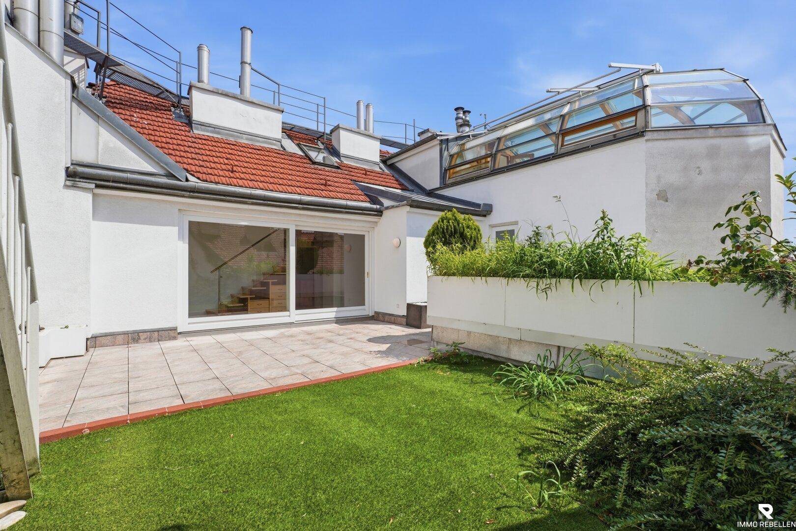 Kleiner Gartenbereich mit Rasen und Pflanzen, angrenzend an eine geflieste Terrasse.