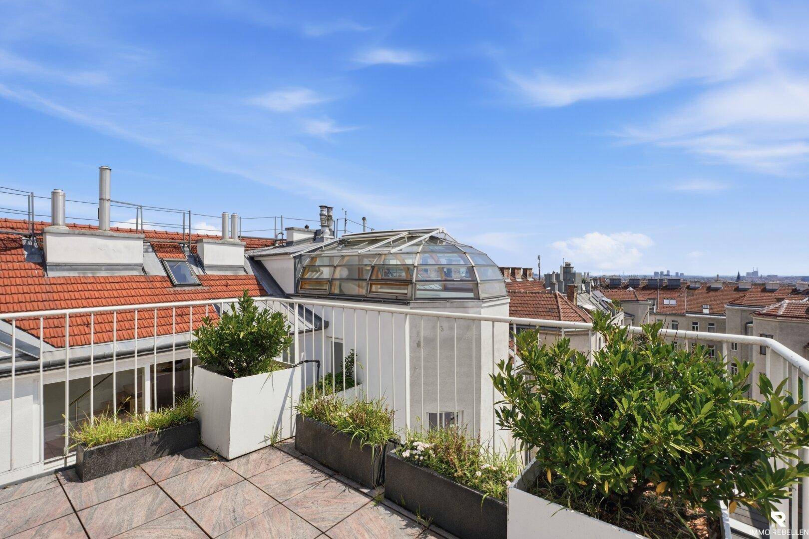 Dachterrasse mit Pflanzkübeln und weitem Blick über die Dächer der Stadt.