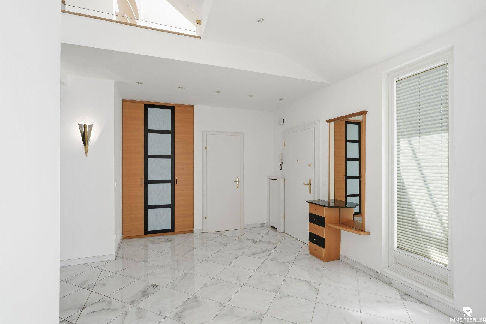 Heller Eingangsbereich mit Marmorfliesen, Einbauschrank und großem Fenster.