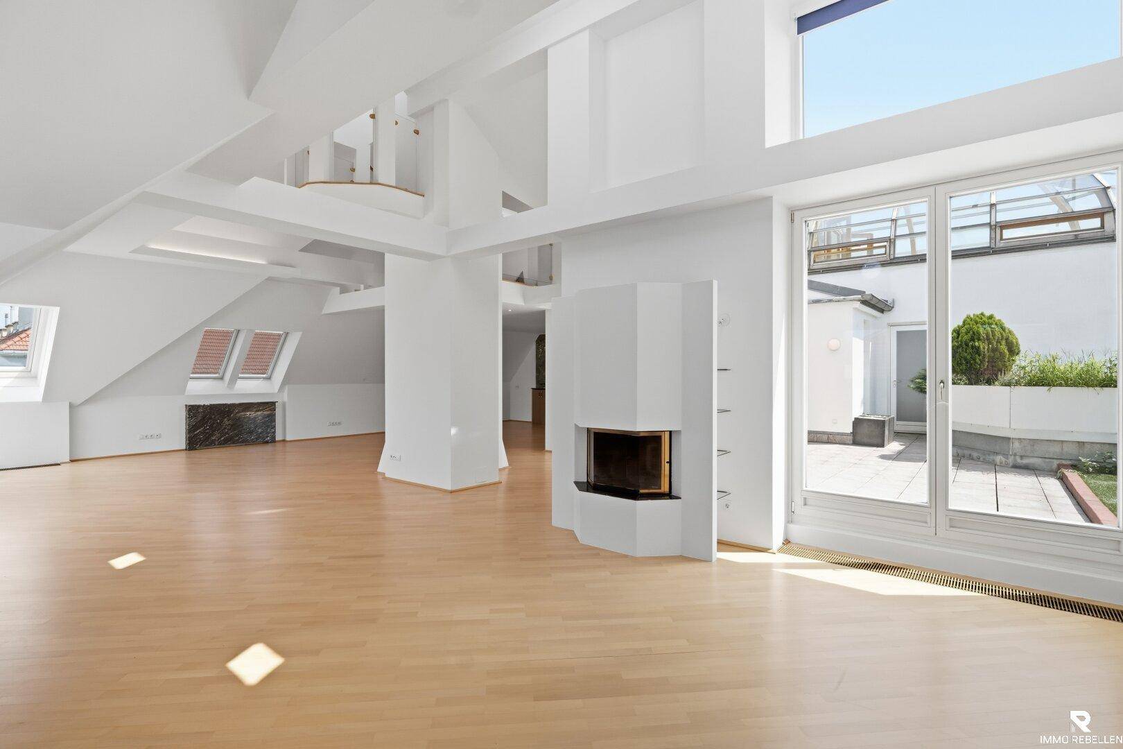 Heller Wohnraum mit Holzboden, Kamin und großen Fenstern mit Zugang zur Terrasse.