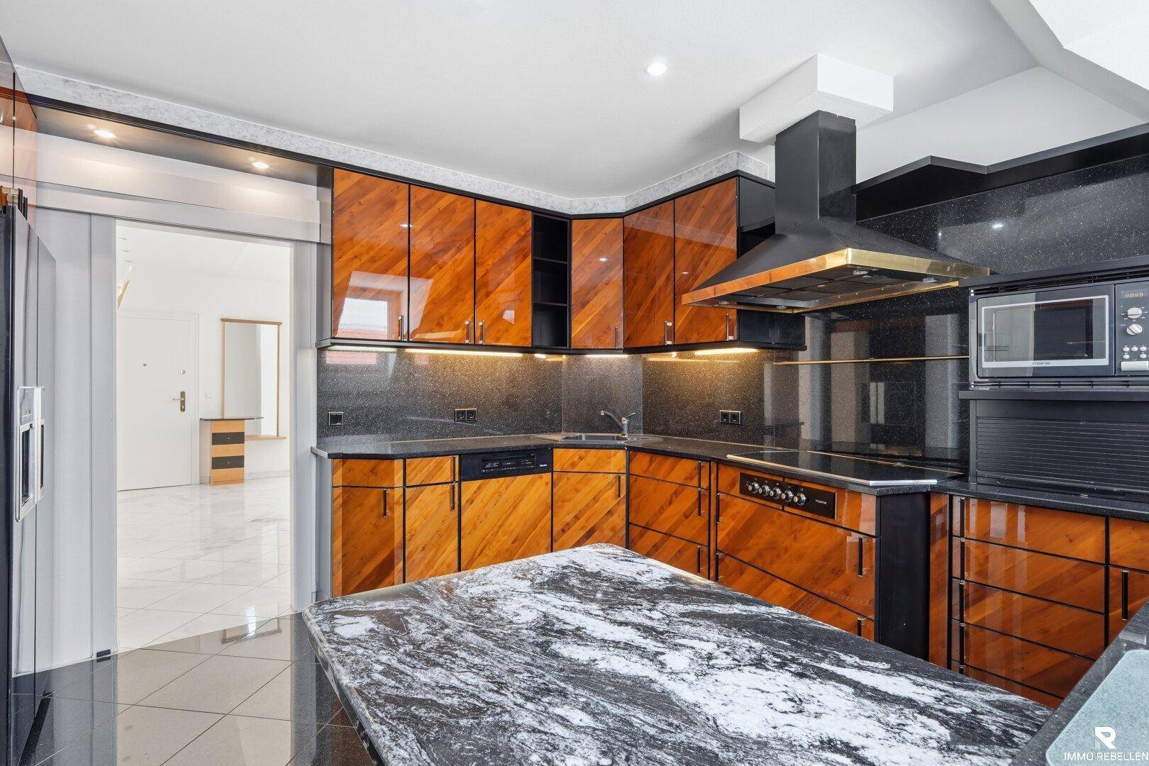 Moderne Küche mit glänzenden Holzfronten, schwarzer Granitarbeitsplatte und integrierten Geräten.