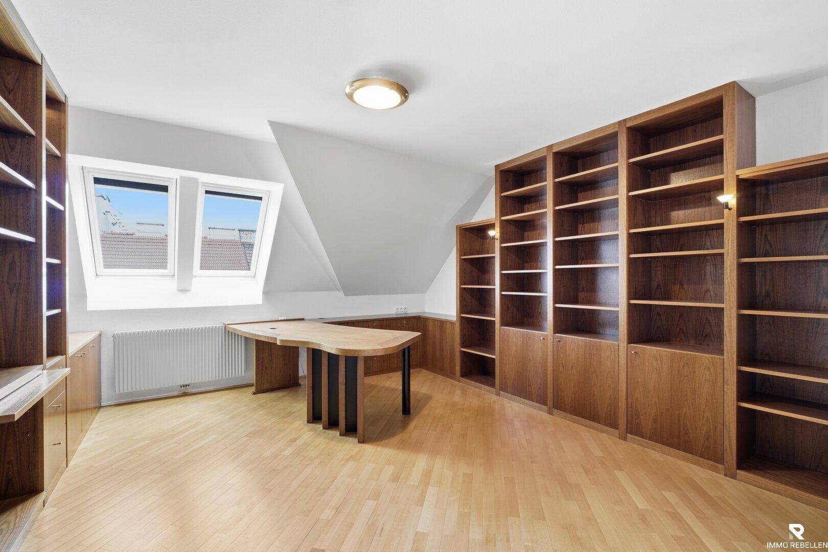 Geräumiges Büro im Dachgeschoss mit Holzboden, Einbauregalen und zwei Dachfenstern.