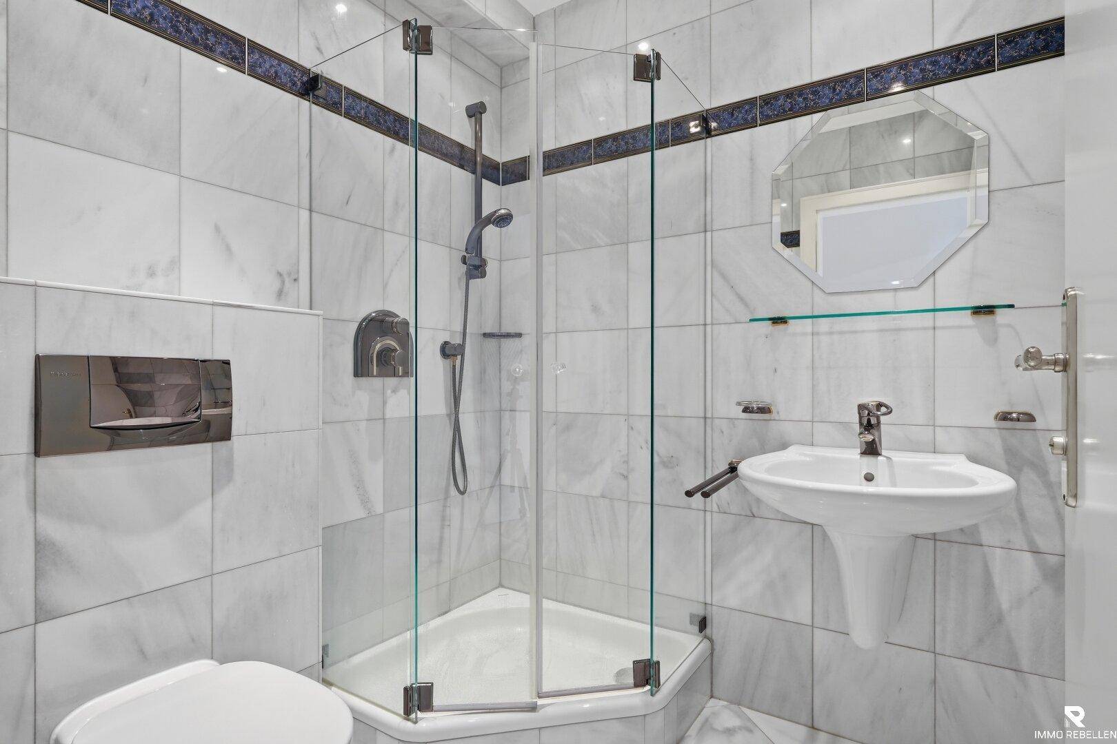 Modernes Badezimmer mit weißen Marmorfliesen, Duschkabine und wandhängendem WC.