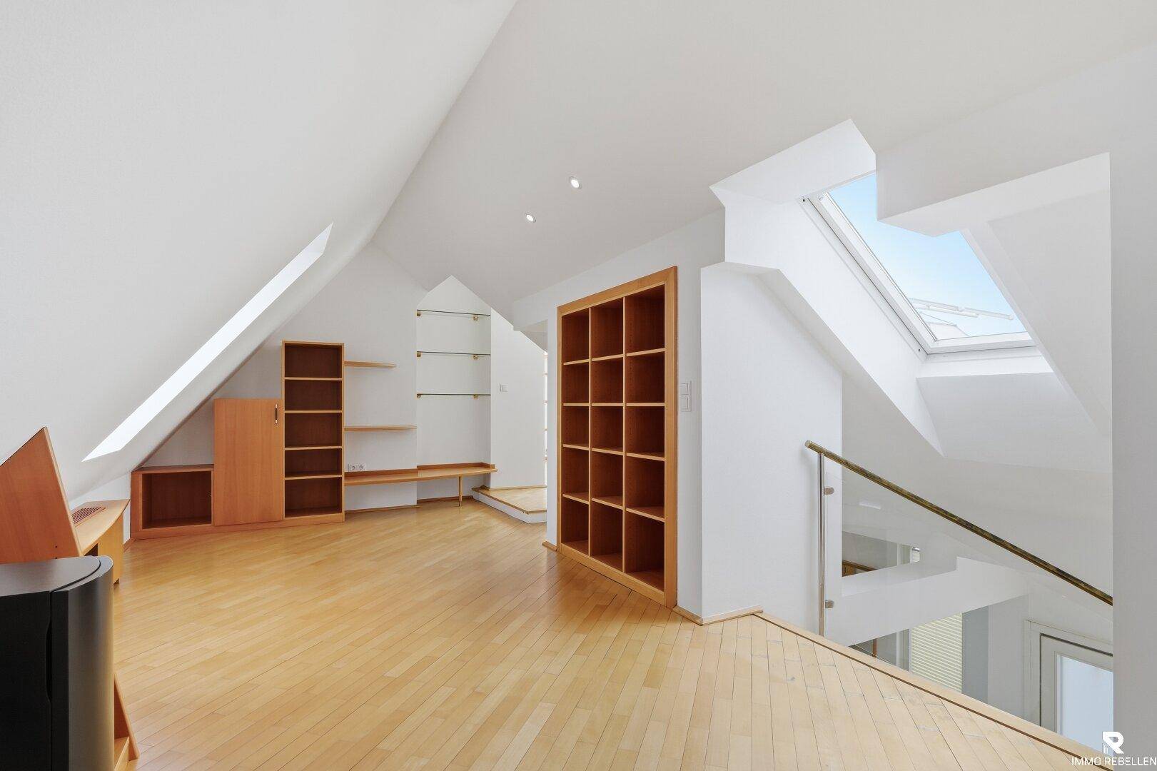 Heller offener Bereich im Dachgeschoss mit Holzregalen, Holzboden und Dachfenster.