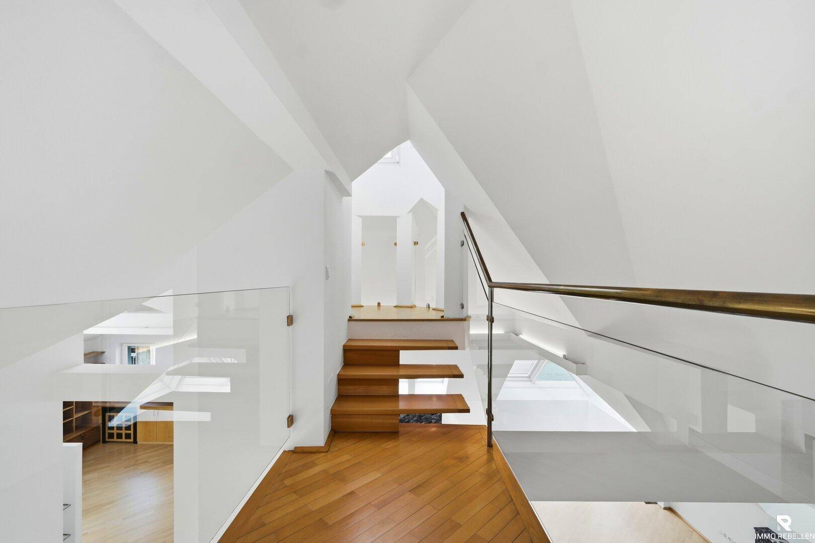 Moderne Treppe mit Holzstufen, Glasgeländer und viel Tageslicht im Dachgeschoss.
