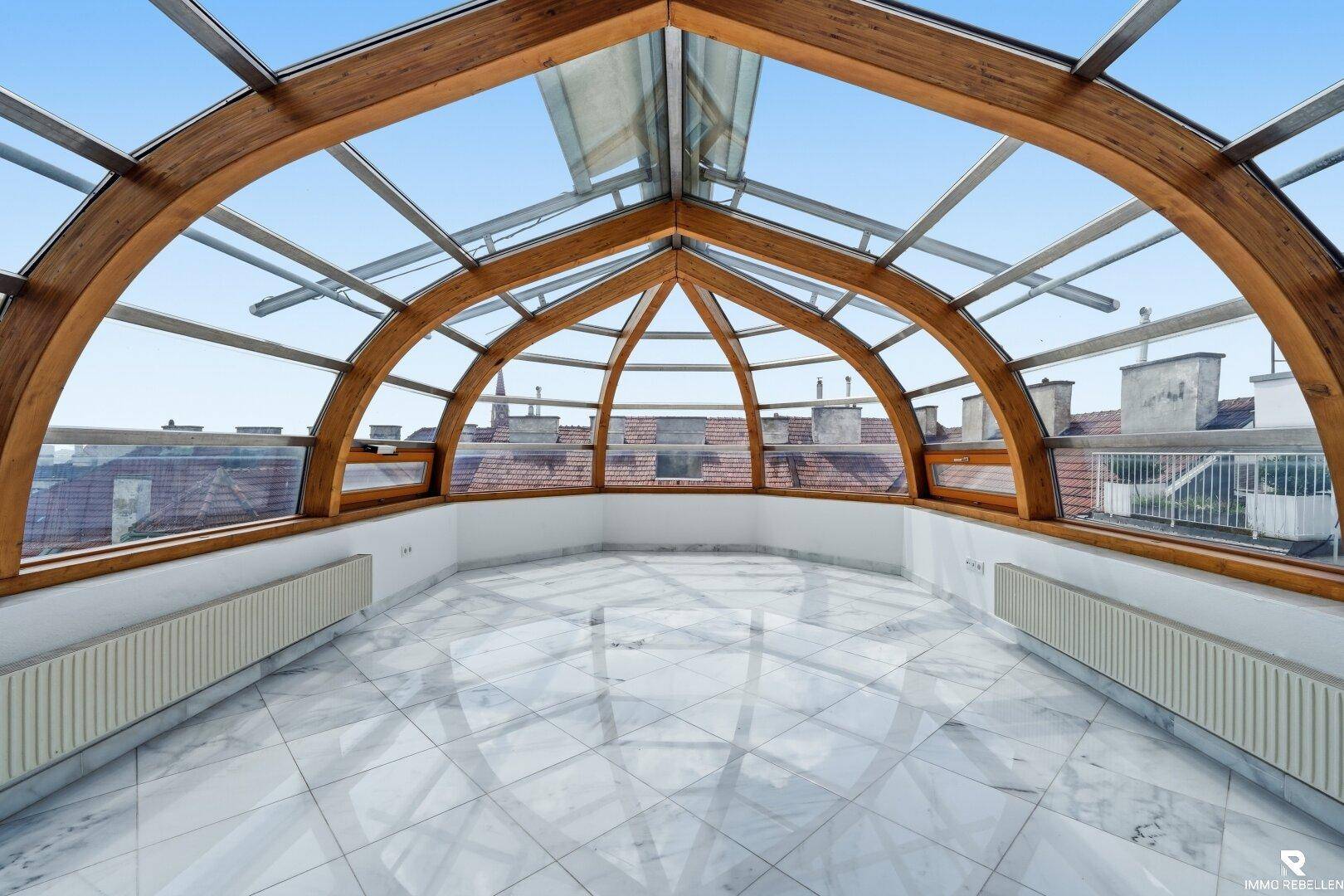 Heller, leerer Wohnraum mit beeindruckender Glaskuppel, Holzbalken und glänzendem Marmorboden.