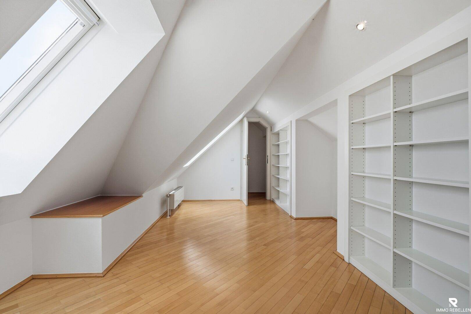 Geräumiger Dachbodenraum mit Holzboden, Einbauregalen und großem Dachfenster.